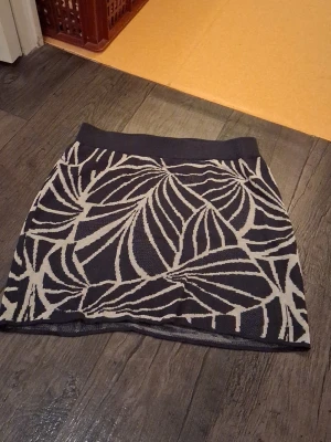 Mönstrad kortkjol från Vila - Säljer en svart och beige kortkjol från Vila med ett coolt grafiskt mönster. Kjolen är stickad och har bred resår i midjan för skön passform. Perfekt att styla med en enkel topp eller hoodie.