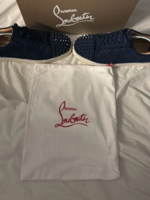 Christian Louboutin svarta sneakers med nitar - Säljer ett par svarta sneakers från Christian Louboutin i mocka med coola svarta nitar på tån och klassisk röd sula. Skorna har snörning och vita sulor, samt kommer med originalkartong och dustbag. Perfekta för dig som vill sticka ut med en lyxig vibe. Du får även med skoblocken som syns på bilden. Kom gärna med prisförslag, priset går att diskuteras😊
