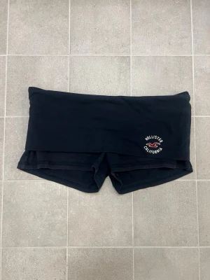 Hollister shorts  - Snygga mörkblå/svarta minishorts från Hollister i storlek S. De är lågmidjade med bred linning och har ett broderat Hollister California-märke framtill. Har ett hål i linningen och är lite urtvättade.