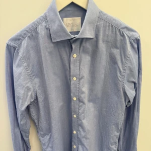 Ljusblå skjorta från Oscar Jacobson stl 40 - Klassisk ljusblå skjorta från Oscar Jacobson med lång ärm och vita knappar. Skjortan har en stilren krage och är gjord i mjuk bomull som känns skön mot soppen. Perfekt till jeans eller chinos för en clean look.