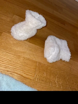 Vita fluffiga tofflor i syntet - Supermysiga vita tofflor med fluffig yta och högre skaft. Perfekta för att hålla fötterna varma hemma.  Storlek 6-12 månader