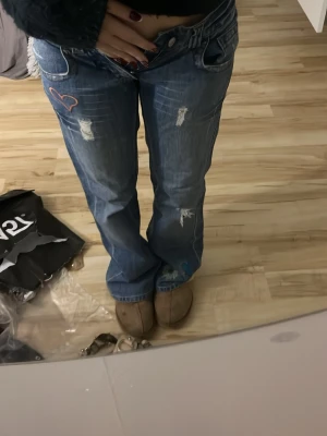 Blå broderade jeans från BlendShe - Säljer ett par blå jeans från BlendShe med broderade detaljer som fåglar, blommor och hjärta. Jeansen har slitningar framtill, raka ben och normal passform. Materialet är 100% bomull och de har klassisk femficksdesign.