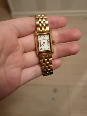 Mockberg guldig rektangulär klocka - Säljer en snygg guldig klocka från Mockberg med rektangulärt ur och klassisk länkarmband. Urtavlan är vit med romerska siffror och gulddetaljer. Perfekt accessoar för att lyfta din outfit. ( psst. Jag har tqgit bort 2 st på amrbandet så att den skulle bli mindre, jag kan skicka me dem delarna om ni köper klockan, jag säljer då jag fick 2 st. Nypris:1600