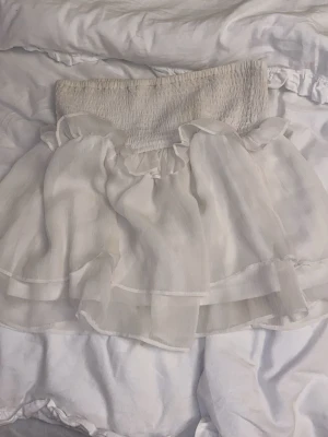 Vit volangkjol med resårmidja - Supersöt vit kortkjol med bred resår i midjan och flera lager volanger. Kjolen har en luftig och lätt känsla, perfekt för varma dagar. Materialet känns tunt och flowy.