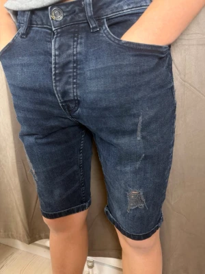 Mörkblå jeansshorts från Denim Co - Säljer ett par mörkblå jeansshorts från Denim Co i slim fit. De har slitna detaljer framtill, klassiska fem fickor och uppvikta benslut. Perfekta för dig som gillar en enkel men ändå edgy stil.