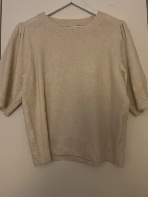 Beige stickad tröja från ONLY - Mysig beige stickad tröja från ONLY med halvlånga puffärmar och ribbade muddar vid ärmslut och nederkant. Perfekt för lager på lager och enkel att matcha med olika stilar. Strl L, aldrig använd! 