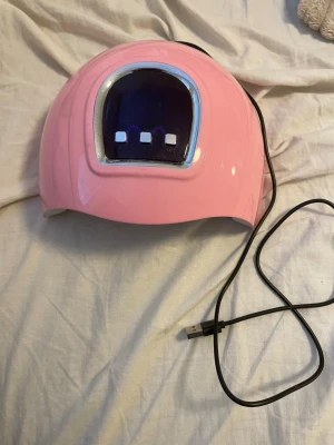 Rosa LED UV-lampa för naglar - Säljer en rosa LED UV-lampa med USB-sladd för att härda gelnagellack. Lampan har tre knappar för olika timerinställningar och flera LED-lampor på insidan för jämn belysning. Perfekt för hemmamanikyr och gelnaglar.