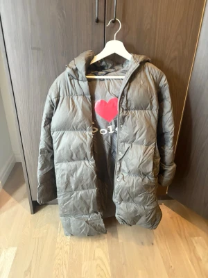 Grå lång pufferjacka från Polo Ralph Lauren - Säljer en lång, grå pufferjacka från Polo Ralph Lauren. Jackan har huva, quiltad design och stängs med både dragkedja och knappar. Perfekt för kalla dagar och riktigt skön att bära. Klassisk och stilren look.