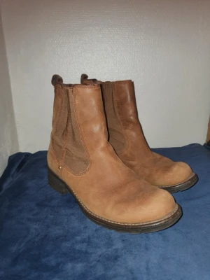 Bruna chelsea boots från Clarks - Säljer ett par klassiska bruna chelsea boots från Clarks i skinn. De har elastiska paneler på sidorna och en robust sula med låg klack. Perfekta till höst och vinter för en stilren look. 4 och en halv i storlek!!