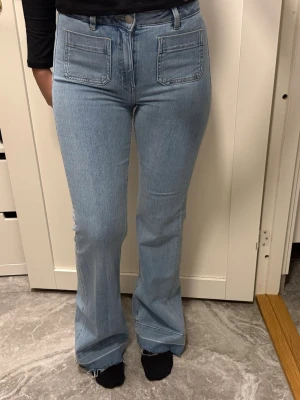 Ljusblå bootcut jeans med fickor - Säljer ett par ljusblå jeans från Bikbok med hög midja och bootcut passform. Jeansen har stora fyrkantiga fickor fram och bak, samt råa kanter längst ner på benen för en trendig look. Tillverkade i mjukt denimtyg som sitter snyggt. Dom är tall girl friendly och formar en snyggt, säljer pga av att jag gått upp i vikt. Storlek W27/L32