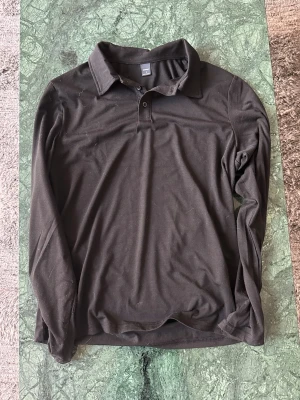 Svart långärmad piké - En svart långärmad henley  med klassisk krage och två knappar vid halsen. Skjortan är enkel och stilren, perfekt för dig som gillar en clean look. Tillverkad i mjuk bomull som känns skön mot huden.