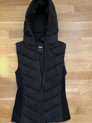 Svart väst från Zara XS - Svart väst från Zara i storlek XS med huva och dragkedja framtill. Snygg och praktisk för höstiga dagar, med en stilren look och bra passform.