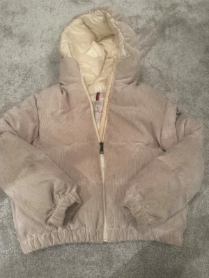 Beige pufferjacka Moncler - Säljer en beige pufferjacka från Moncler med luva och dragkedja. Jackan har ett quiltat innerfoder i ljus färg och klassisk Moncler-logga på ärmen. Perfekt för kyliga dagar.
