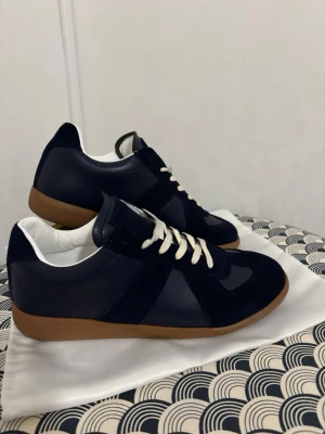 Mörkblå sneakers med mockadetaljer - Snygga mörkblå sneakers med ovandel i både mocka och skinn, vita snören och klassisk brun gummisula. Skorna har en stilren och sportig look med rund tå och lågt skaft. Perfekta för dig som gillar en clean och tidlös stil. Priset kan diskuteras🥂