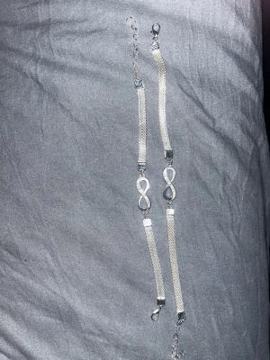 Fotlänk & armband - Två stilrena armband & Fotlänk i silverfärg med mesh-länk och dekorativ infinity-symbol i mitten. Armbanden har justerbar kedja och smidigt spänne. Perfekt accessoar för att lyfta din outfit med en elegant touch.