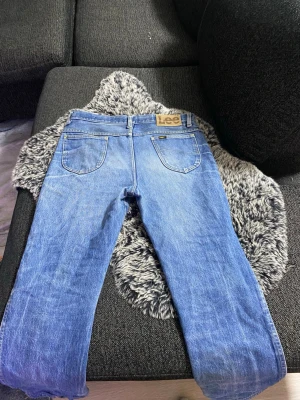 Blå Lee jeans med raka ben - Säljer ett par klassiska blå jeans från Lee med raka ben och normal passform. Jeansen har fem fickor, bälteshällor och Lee-logga på bakfickan. Materialet är slitstarkt denim i bomull och färgen är ljusblå med snygga slitningar.