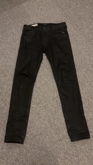 Svarta Replay Anbass jeans  - Säljer ett par svarta Replay Anbass jeans i slim fit i storlek 30/32. Klassisk femficksmodell med snygga detaljer och diskret logga på fickan. Jeansen är tillverkade i stretchigt material för extra komfort. Skick 9/10. Pris kan diskuteras!