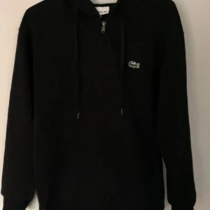 Svart hoodie från Lacoste med dragkedja - Svart hoodie från Lacoste passar XS och S ifall man vill ha tajt 
