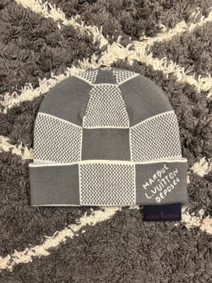 L rutig mössa - Grå och vit mössa från L med rutigt mönster och broderad text 'Marque L. V Déposée' på kanten. Stickad i lyxig blandning av kashmir, ull och silke. 