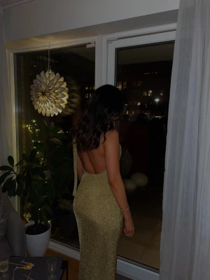 Nyårsafton klänning  - Säljer denna superfina långklänningen i guld. Perfekt till nyår eller andra festliga tillställningar!Klänningen har hög hals, är ärmlös och har en snygg öppen rygg. Figurnära passform och slits nertill för extra rörelsefrihet. Perfekt för dig som vill sticka ut på festen!