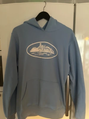 Ljus blå CORTEIZ hoodie - Säljer en fet hoodie från Corteiz för endast 650kr! Hoodien är ljus blå och är super tjock, den passar perfekt till vinter väder! Har använt den ett par gånger och har inga fläckar.