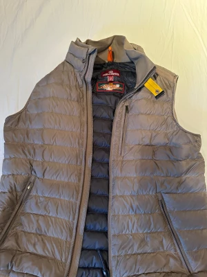 Parajumpers väst - Säljer en superlätt beige dunväst från Parajumpers i storlek M. Västen har quiltad design, hög krage och dragkedjor på fickorna. Perfekt för lager-på-lager och har en snygg gul detalj vid axeln. Klassisk och clean look som funkar till det mesta.