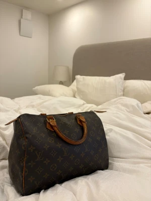 Louis Vuitton Speedy 30 - Dags att sälja denna underbara (!!!) väska som funkar till allt. Har köpt väskan vintage via Vesitaire Collective där experter kontrollerar äktheten. Överlag är väskan väldigt rymlig och får plats med mycket, finns även en liten ficka inuti. Hänglås med tillhörande nyckel kommer även med. Tveka inte på att höra av dig om du har frågor 🩷