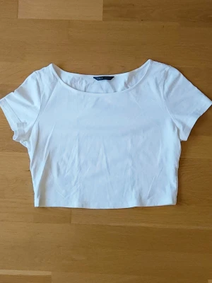 Vit croptop - En stilren vit croptop från med rund halsringning och korta ärmar. Toppen är enkel och har en clean look, perfekt att matcha med jeans eller kjol. Känns mer som en L än en XL.