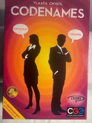 Vlaada Chvátil Codenames Ordspelet - Vlaada Chvátil Codenames är ett ordspel som innehåller spelkort, brickor och regler. Spelet är designat för att spelas i lag och fokuserar på att hitta ord kopplade till ledtrådar. Spelet är lämpligt för flera spelare och innehåller komponenter i olika färger och teman.