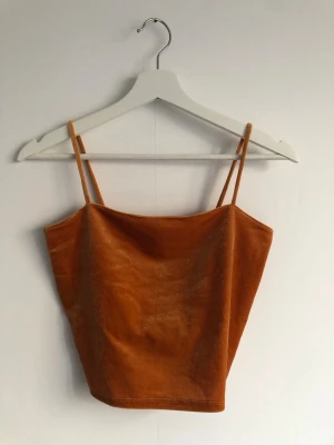 Orangeguldig top i sammetstyg - Top från Gina tricot. Storlek XS. Dubbelt tyg över brösten som gör det skönare att inte ha bh under. Mycket fint skick, inget att anmärka på.  