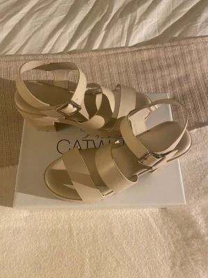 Beige sandaler med klack från Catwalk - Snygga beige sandaler från Catwalk med breda remmar och justerbart spänne i silver. Skorna har en stabil blockklack och plattformsula för extra komfort. Tillverkade i syntetmaterial med öppen tå och modern design, perfekta för att lyfta din sommarstil. Säljer då dom är för små!🙌❤️