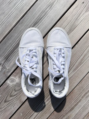 Vita Vans Old Skool, använda 1 gång, storlek 39 - Klassiska Vans Old Skool sneakers med lågt skaft, rund tå och platt sula. Skorna har snörning och är tillverkade i canvas och syntet. Använda 1 gång. Önskar du veta exakta mått? Tveka inte att höra av dig!