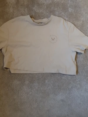 Beige croppad t-shirt från SOC - Beige croppad t-shirt från SOC med rund hals och korta ärmar. T-shirten har en enkel design med liten logga på bröstet och är gjord i mjuk bomull. Perfekt för en avslappnad och sportig stil.