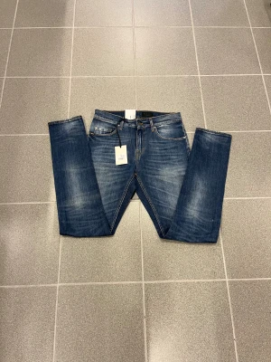 Blå tiger of sweden jeans W29 L34 - Snygga blå jeans med  smal fot. Klassisk femficksmodell med orangea sömmar och slitningar på låren och knäna för en cool look. Passar dig som gillar tidlös stil och vill ha jeans med lite attityd. Från tiger of sweden 