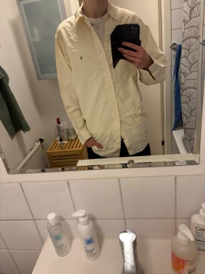 Randig Ljusgul skjorta från Ralph Lauren - Säljer en ljusgul skjorta från Ralph Lauren med klassisk krage och broderad logga på bröstet. Skjortan har diskreta ränder, knäppning framtill och långa ärmar. Säljer så pass billigt eftersom att det är en stor storlek (XXL om inte ens lite större) perfekt som julklapp till farsan!