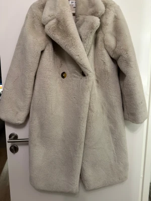 Beige pälsjacka från Dry Lake stl s  - Supermjuk och fluffig beige pälsjacka från Dry Lake i stl s med bred krage och stora knappar. Jackan är helfodrad i satinliknande material och har en rak, oversized passform. Pälsjackan är använd endast engång och är som ny. Säljs för den inte kommer till användning och bara legat i garderoben.  