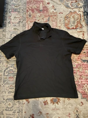 Svart kortärmad pikétröja från Zara - Svart kortärmad pikétröja från Zara med knappar vid halsen. Tröjan är i mjuk bomull. Helt ny och oanvänd. 