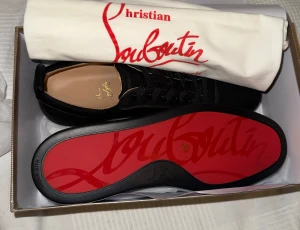 Svarta sneakers från Christian Louboutin - Snygga svarta sneakers från Christian Louboutin med klassisk röd sula och guldfärgad logga på innersulan. Skorna har rund tå, platt sula och är tillverkade i mjuk mocka med svarta snören. Perfekt för dig som vill ha en lyxig och stilren look.
