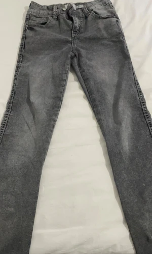 Grå bootcut jeans  - Snygga grå jeans med bootcut passform och klassisk femficksdesign. Jeansen har en lätt tvättad look och är tillverkade i mjukt denimtyg som ger en skön känsla. Perfekta för dig som gillar en avslappnad stil med lite edge.
