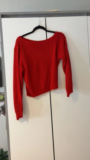 Röd stickad tröja med bred hals - Snygg röd stickad tröja med bred halsringning och lång ärm. Modellen är lite croppad och har en ribbad struktur som ger en cool och modern vibe. Perfekt att matcha med jeans eller kjol för en trendig look.