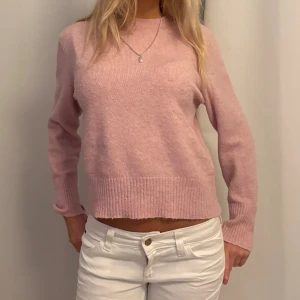 Ljusrosa stickad tröja med rund hals - Superfin ljusrosa stickad tröja med rund hals och ribbade muddar. Tröjan har en klassisk passform och är långärmad, perfekt att matcha med jeans eller kjol. Mjuk och skön, passar perfekt för kyligare dagar.