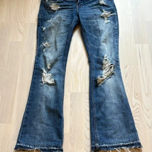 Bootcut jeans från Abercrombie & Fitch - Säljer ett par blå bootcut jeans från Abercrombie & Fitch med slitna detaljer och trasiga partier på både fram- och baksida. Sjukt snygga vintage jeans i bra skick med tanke på ålder! köpta på vinted, tyvärr lite för små för mig  Storlek 0, alltså 32/XS Midjemått: 38cm Innerbensmått: 73cm ytterbensmått: 95cm Benöppning: 23cm