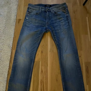 Replay Newbill blå jeans, stl 31 - Säljer ett par Replay Newbill jeans i klassisk blå tvätt med snygga slitningar och detaljer. Jeansen har raka ben, fem fickor och tydliga Replay-loggor. Perfekta för dig som gillar en avslappnad och tidlös look. Dom har slitningar vilket ger dom en extra utstickande look!