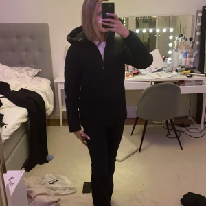 Svart pufferjacka från Everest - Säljer en svart pufferjacka från Everset med huva och dragkedja framtill. Jackan har en stilren look och är perfekt för kyligare dagar. Klassisk passform och diskret logga på ärmen. Passar dig som vill ha en enkel men snygg vinterjacka.