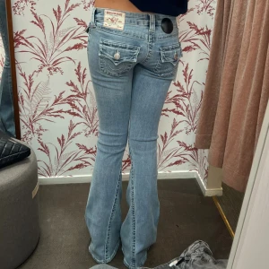 True religion joey jeans - Superpopulära ljusblå jeans från True Religion med klassiska kontrastsömmar och ikoniska fickdetaljer bak. Modellen Joey och har bootcut-ben och en så fin låg midja. Storlek W25 men passar xxs/xs/s. Lite slitna längst  ner på baksidan men är inget som man tänker på så de är i bra skick❤️Midjemåttet är 38 cm och innerbenslängen är 82 cm🫶🏻