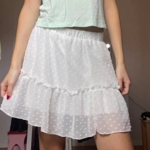 Vit volangkjol🤍 - Supersöt vit kortkjol med volang och små prickar i tyget. Kjolen har ett tunt, transparent ytterlager med strukturprickar och ett mjukt innerfoder. Resår i midjan gör den bekväm och lätt att bära. Perfekt för dig som vill ha en kjol till våren och sommaren✨