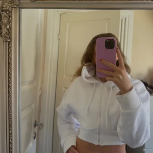 Vit croppad hoodie från LXA - Säljer en vit croppad hoodie från LXA med dragkedja framtill och snörning i huvan. Tröjan har oversized passform, långa ärmar och bred mudd i midjan. 