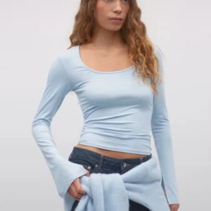 Ljusblå långärmad topp Gina Tricot - Superfin ljusblå långärmad topp från Gina Tricot med rundad, djup urringning. Modellen är tight och croppad, perfekt att styla med jeans eller kjol. Tunt och stretchigt material som känns skönt mot huden.