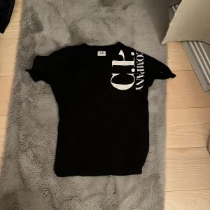 Svart C.P. Company t-shirt med tryck - Svart t-shirt från C.P. Company med stort vitt tryck på framsidan och ryggen. Klassisk rund hals och korta ärmar. T-shirten är i mjuk bomull och har en clean, modern vibe med tydlig logga som sticker ut.