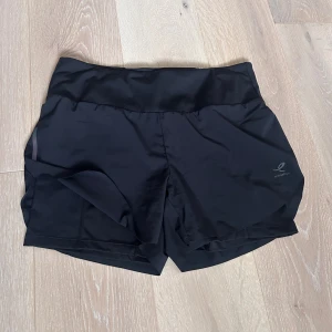 Svarta träningsshorts  - Svarta Energetics träningsshorts med åtsittande innershorts under! Tillverkade av lätt, stretchig och mycket andningsbar polyester. Perfekta för löpning eller gymmet, med en diskret logotyp på sidan och en innerficka för småsaker.